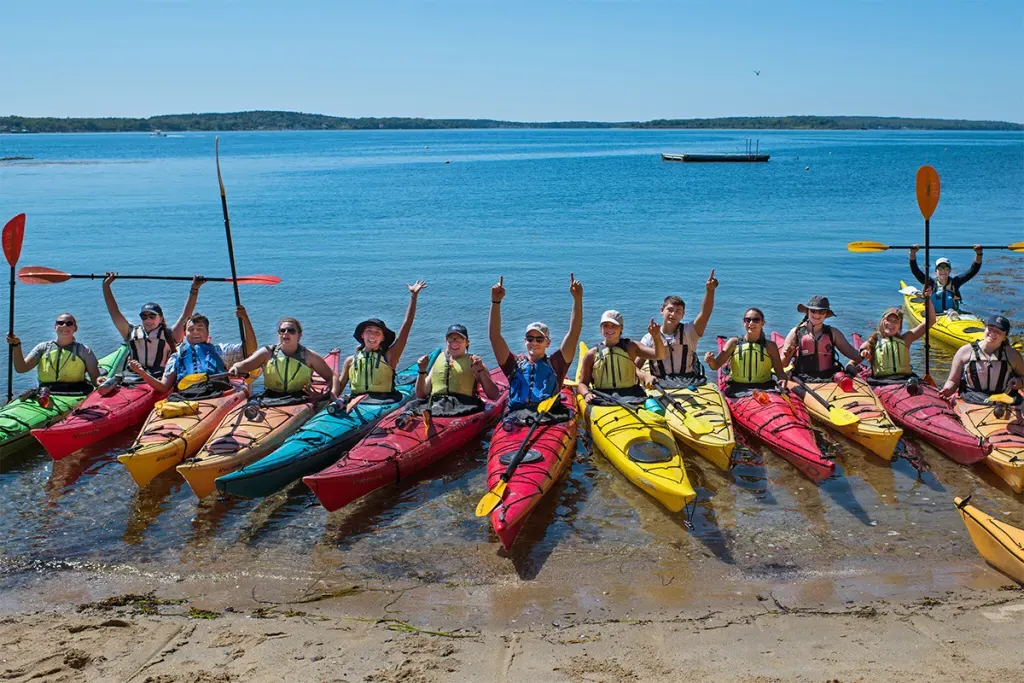 A group of students sitting in kayaks on the shore