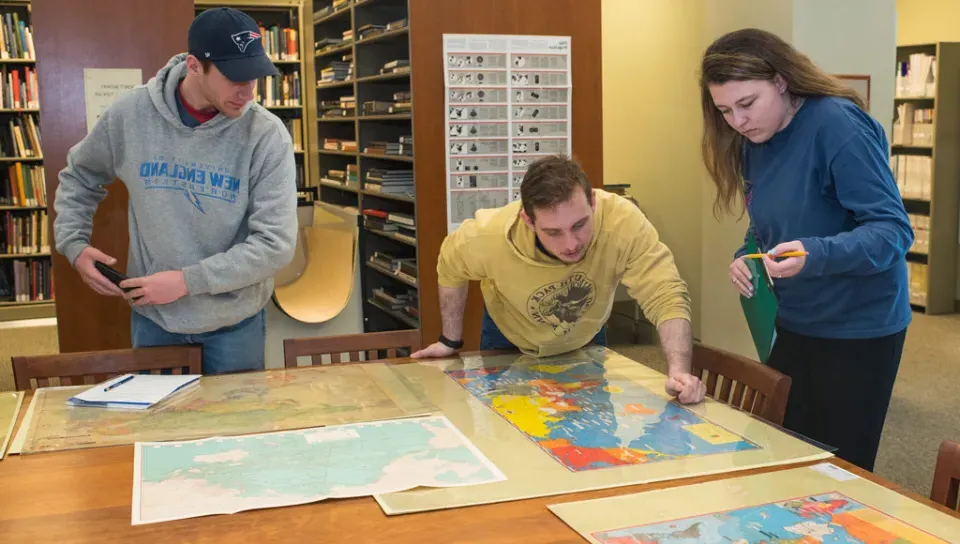 A group of students look at old maps of the United States laid out on a wooden table