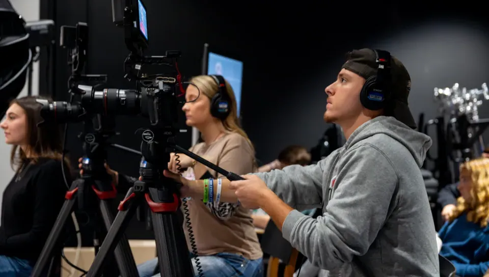 A student runs a video camera during a mock interview