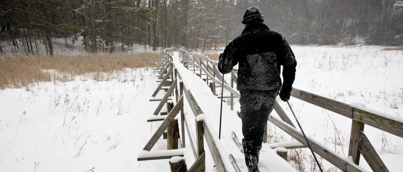 A man cross-country skis over a snow-covered bridge