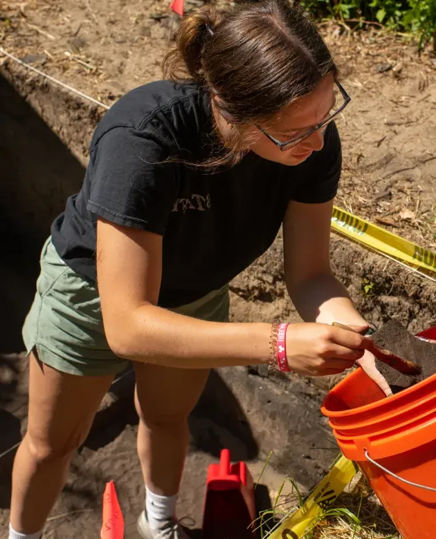 A student brushes dirt off an artifact found in a dig site