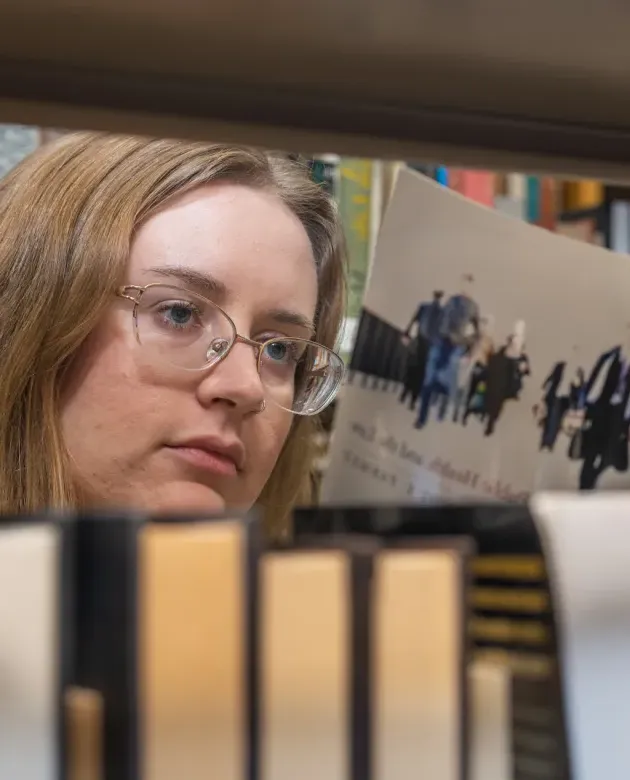 A student reading a book amongst library stacks