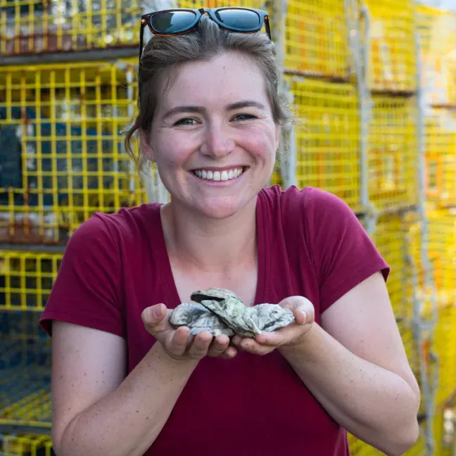 a students holds two handfuls of clams in front of fishing traps