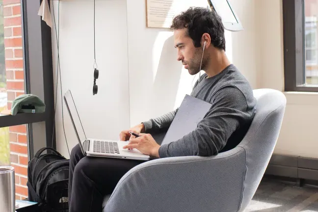 a student sits in an armchair working on a laptop